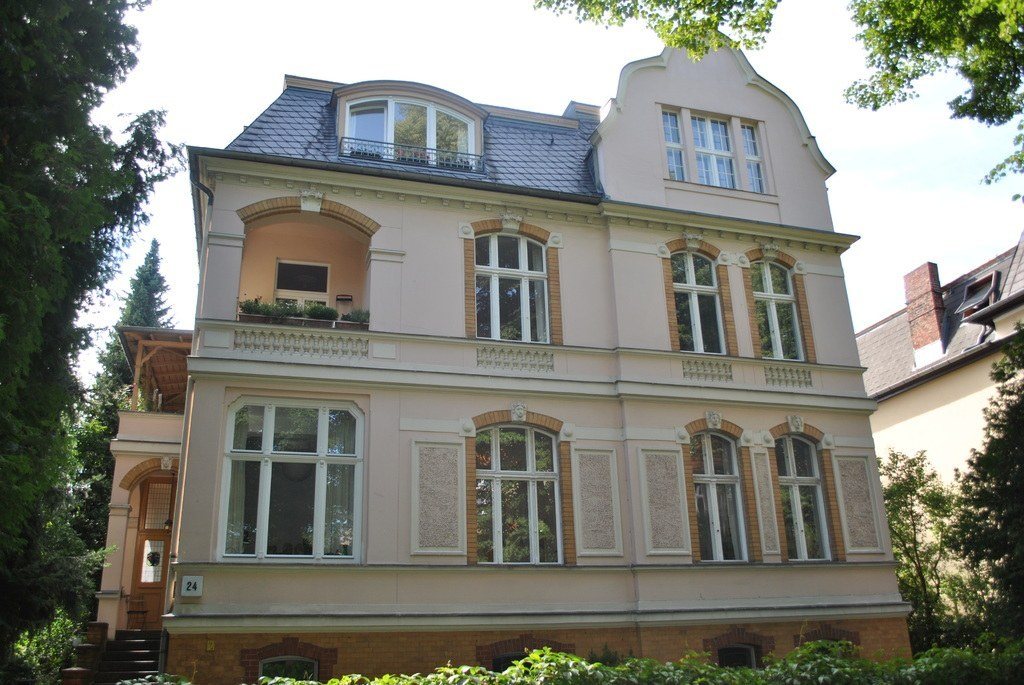 Elegant cream townhouse with tall windows behind a leafy garden